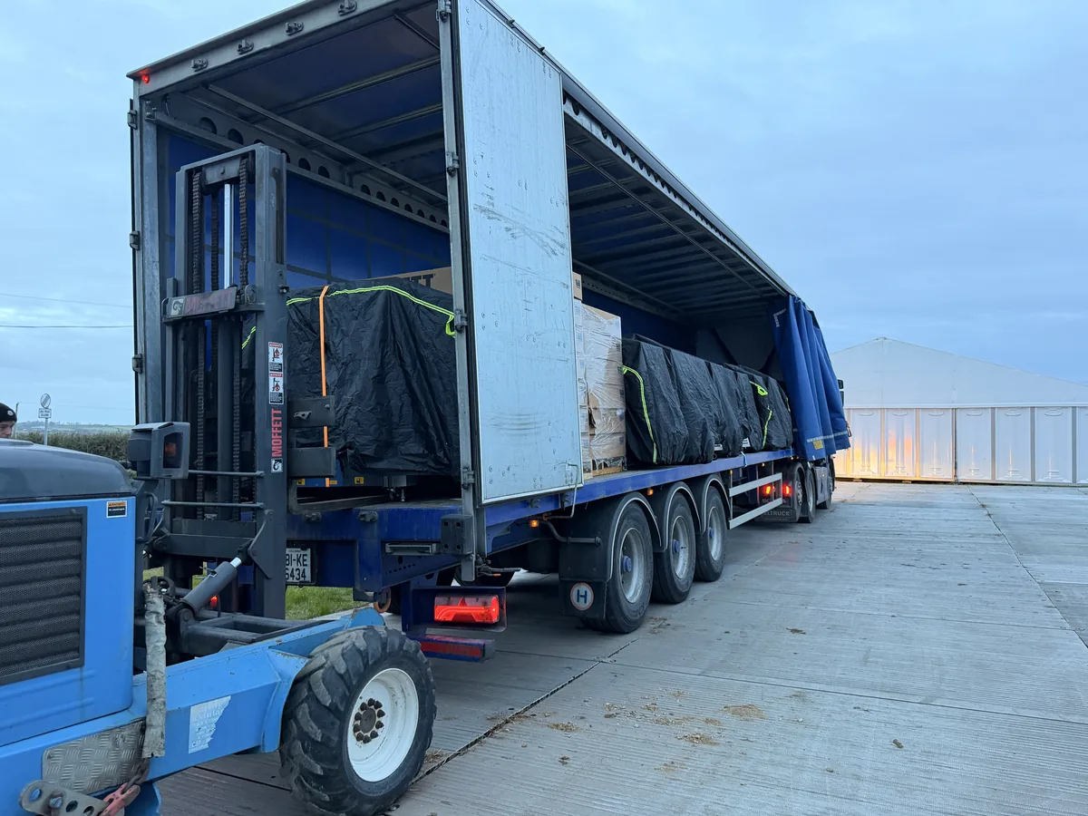 Screening equipment being unloaded from a curtainside trailer by a Moffett forklift at dawn beside the event marquees