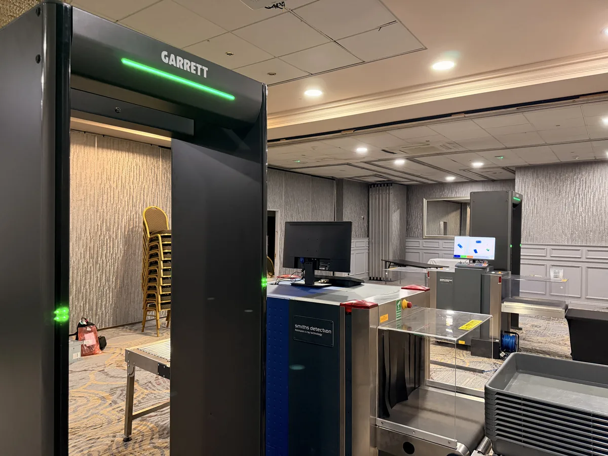Indoor screening checkpoint with Garrett walk-through metal detectors and Smiths Detection X-ray machines set up in a function room