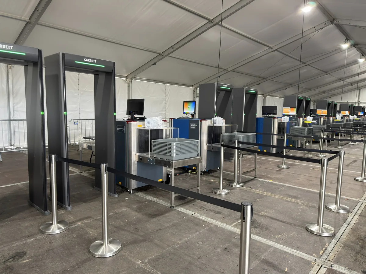 Garrett walk-through metal detectors and Smiths Detection X-ray lanes with queue barriers and tray stacks at an Irish Open park and ride screening site