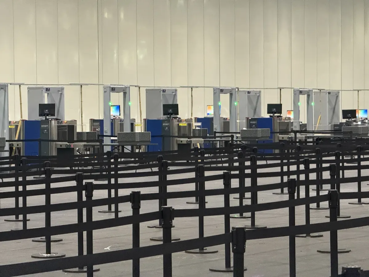 A row of hired walk-through metal detectors and queue lanes inside a large event hall